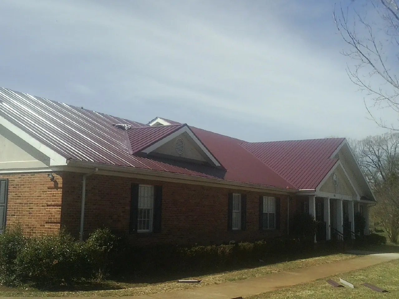 Red metal roof with gabled entries on a long brick building, from a Hail Damage Roof Repair job in Buxton