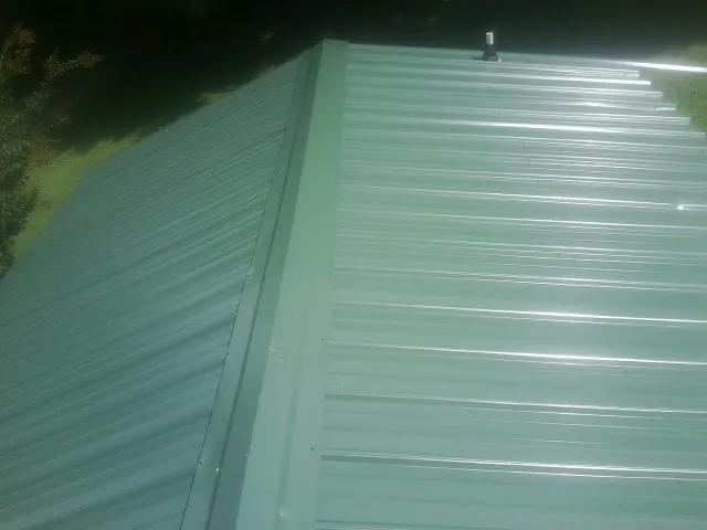 New green metal panels meeting at the ridge of a roof — Flat Roof Repair work by our crew in Buxton