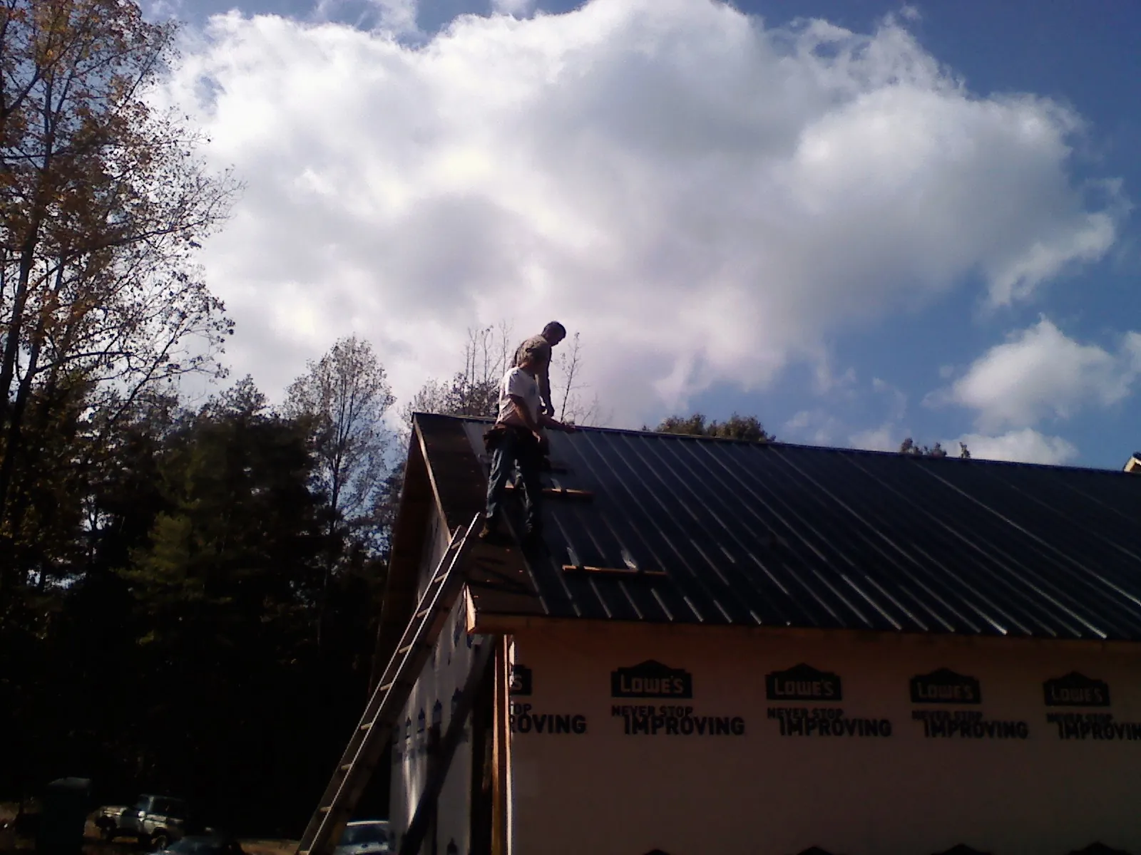 Roofer fastening dark metal panels high against a cloudy sky, from a Roof Inspection job in Buxton